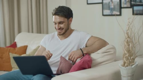 Man Works on Laptop at Home on Couch