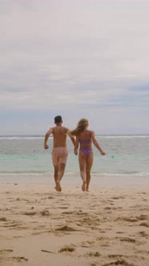 Couple Holding Hands Running on Sandy Beach Toward Ocean