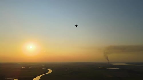 Vista aérea de um grande balão de ar quente sobrevoando a paisagem rural ao pôr do sol