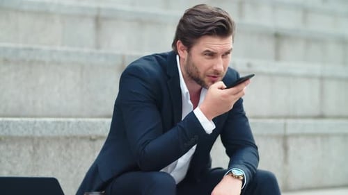 Serious Businessman Recording Voice Message on Cellphone in City. Sad Professional Using