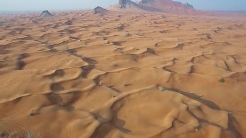 Aerial View of Vast Desert Dunes and Rugged Mountain Peaks in 4K