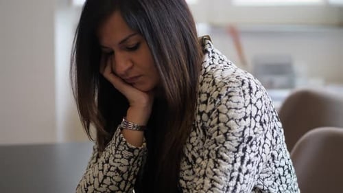 Sad young woman sitting alone at home feeling headache depression