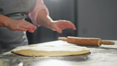 Closeup of Female Hands Rolling Out Dough with a Rolling Pin on the Table