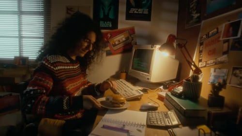 Young Adult Typing at Computer Eats a Burger