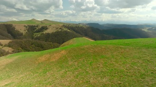 Top view of hills with green grass and sparse forest