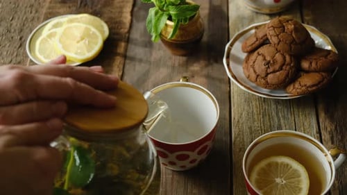 Hands Pouring Brewed Green Tea with Lemon From Teapot