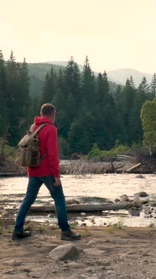 Hiker Standing with Raised Arms Near Mountain River in Forest