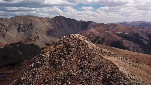 Rotating aerial shot of a rocky red mountain peak on a sunny summer day