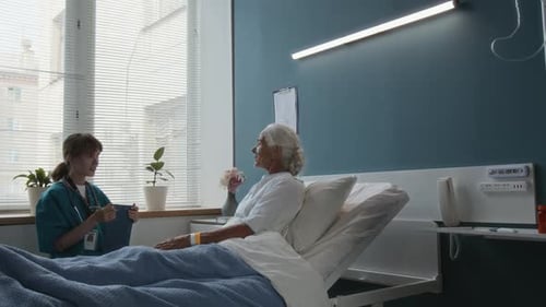 Cheerful Nurse Having Conversation with Senior Female Patient in Hospital Ward