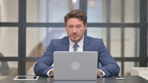 Businessman Working on Laptop in Bright Office