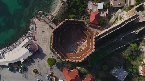 Vídeo aéreo de una histórica fortaleza costera con una torre roja en una bahía azul en un lugar despejado y soleado