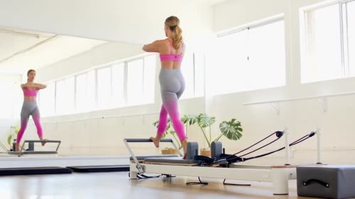 Young Caucasian woman exercises on a Pilates reformer in a bright studio