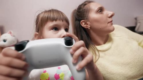 Wide Angle Little Girl is Playing Video Games on a Console with Her Mom Holding a Modern Controller