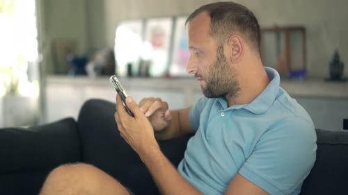 Man Uses Mobile Phone on Sofa at Home