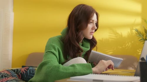 Woman Writes in Notebook While Using Laptop