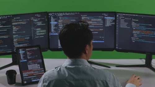 Asian Man Working With Tablet While Write Code With Multiple Computer Screens In Green Screen