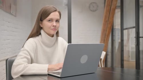 Woman Smiling While Working on Laptop Indoors