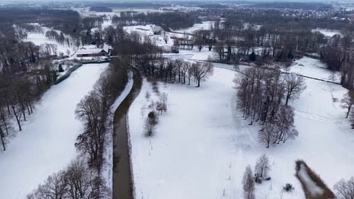Aerial winter view of a winding river flowing through snowy fields and forests with scattered houses