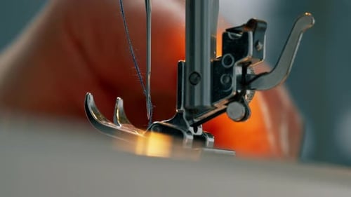 Primer plano en un taller de costura: el hilo se inserta en una aguja de una máquina