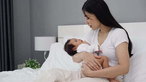 mother holding and talking with her newborn baby on a bed