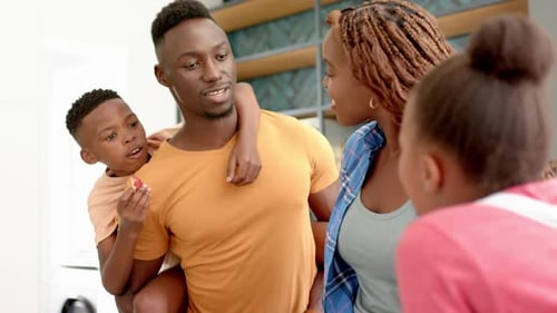 Padre sosteniendo a su hijo sobre los hombros, sonriendo y hablando con la madre y la hija