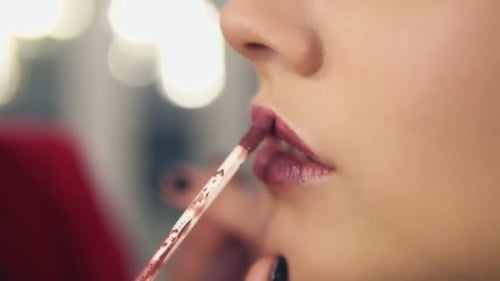 Closeup view of a professional makeup artist applying lipstick on model's lips