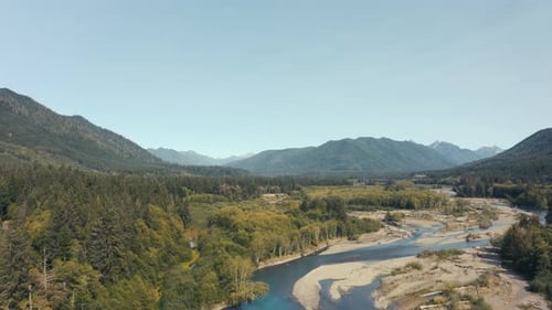 Gorgeous aerial drone shot of a blue mountain river cutting across a sandy beach floor.
