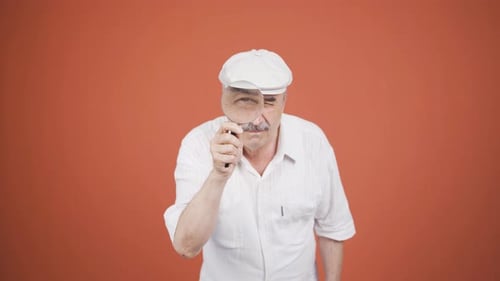 Man Looks Through Magnifying Glass Against Orange Backdrop