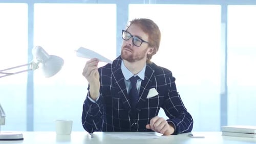 Man Sits at Desk With Paper Airplane