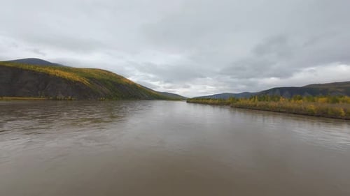 Experience the tranquility of a winding river framed by majestic mountains and colorful autumn trees
