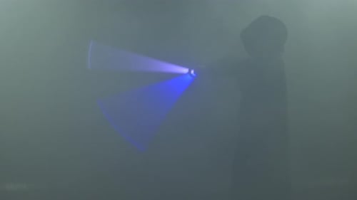 Young Man in Jedi Cosplay Costume with Lightsaber Battle on Black Background in Smoke and Rain Slow