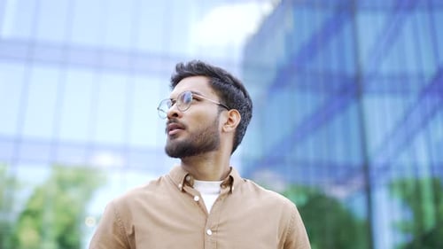 Handsome businessman looks around standing on street near office building. Successful man