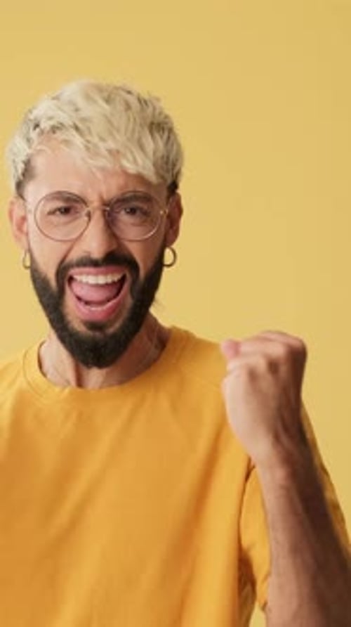 Man wins, waves hands triumphantly, looking at camera isolated on yellow background in studio