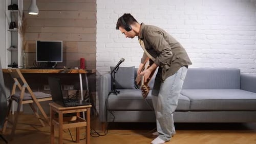 Young Man Wearing Headphones Sitting on a Sofa in His Home Studio Preparing to Record Acoustic