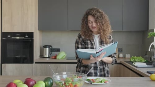 Woman Reads Recipe Book While Making Salad