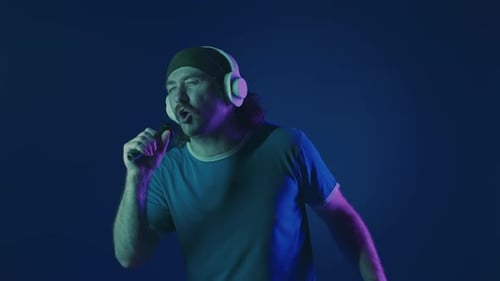 A Mustachioed Man in White Wireless Headphones Dances and Sings Into a Microphone Woman in Studio on