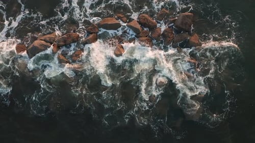 Aerial top down, ocean wave crashing into rocks creating foam