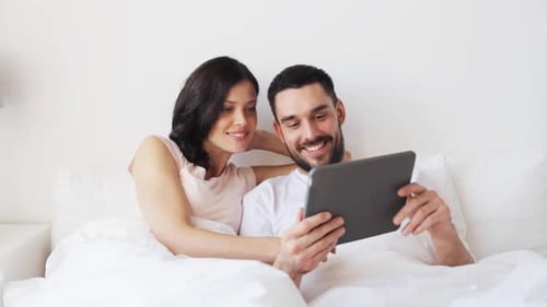 Technologie, Internet und Menschen: Lächelndes Paar im Bett mit Tablet