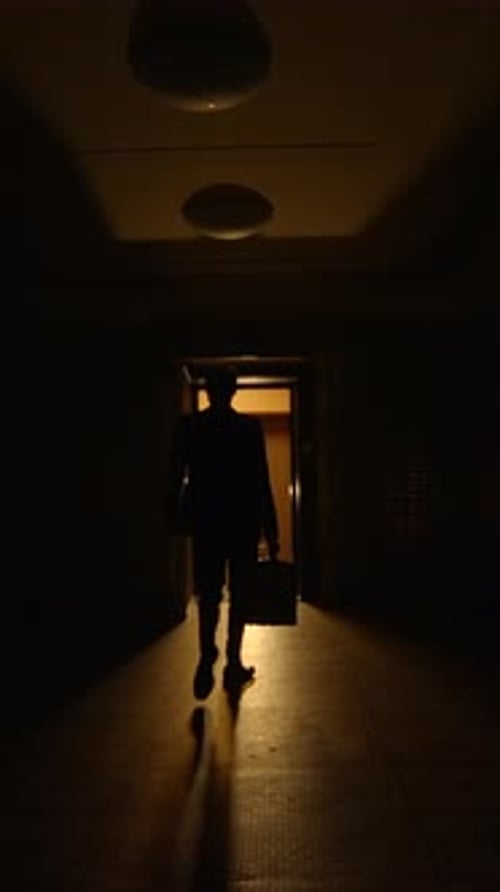 Man Walks Toward Metal Gate in Dark Corridor