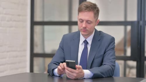 Young Businessman Browsing Internet on Phone in Office