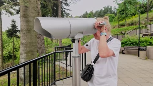 Woman looks through telescope at scenic lookout observation point