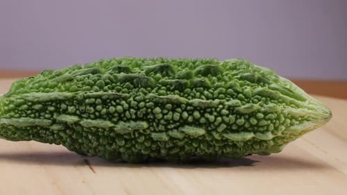 Une gourde amère, un légume souvent utilisé comme ingrédient en cuisine, est posée sur une table en bois.