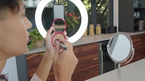 Person Applying Makeup Using Brush in Modern Kitchen