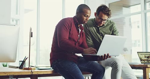 4k video footage of two cheerful young businessmen working on a computer together in the office