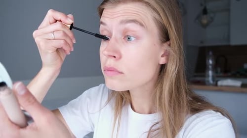 Woman Applies Mascara with Handheld Mirror