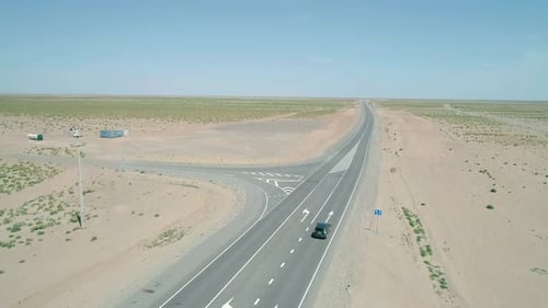 Aerial Panorama a Car Driving on a Highway Road Between Sands with Little Green Grass Bushes