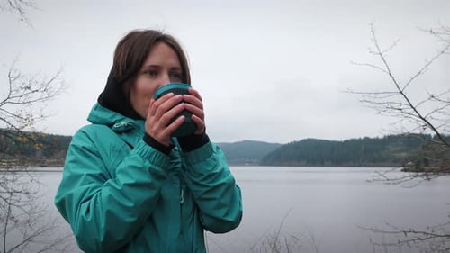 Woman with mug drinking tea outdoors near lake