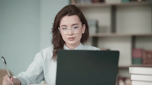 Young female student studying in library with laptop