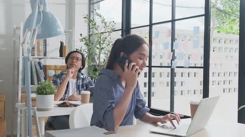 Two young Asian startup partners are working in a casual small business office.