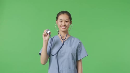 Asian Female Doctor With Stethoscope Crossing Her Arms And Smiling On Green Screen Background